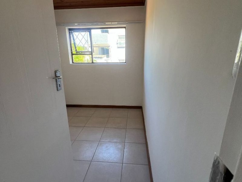 A compact, empty bedroom featuring ceramic floor tiles and a timber tongue and groove ceiling, offering a neutral canvas for potential interior design updates.