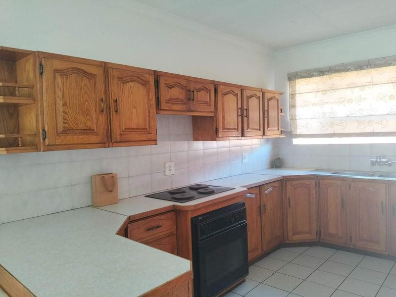 A functional kitchen featuring traditional wooden cabinetry, laminate countertops, a built-in oven with electric hob, and tiled flooring.