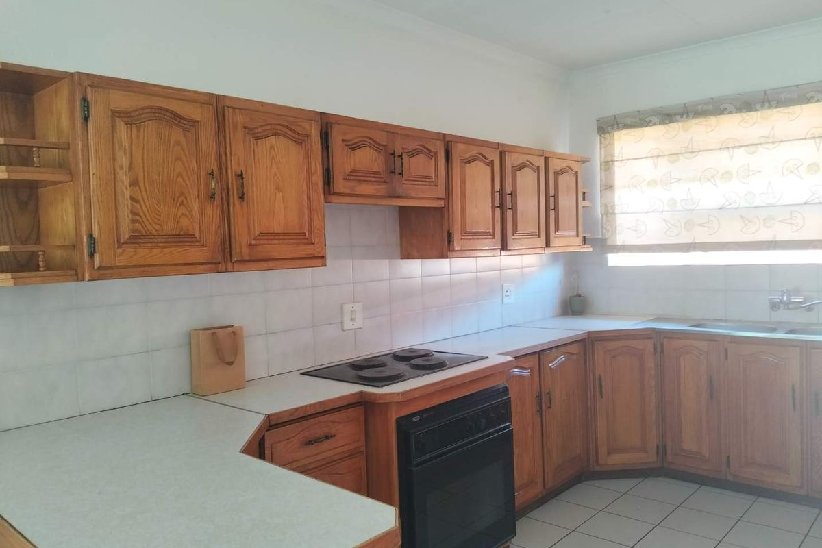 A functional kitchen featuring traditional wooden cabinetry, laminate countertops, a built-in oven with electric hob, and tiled flooring.