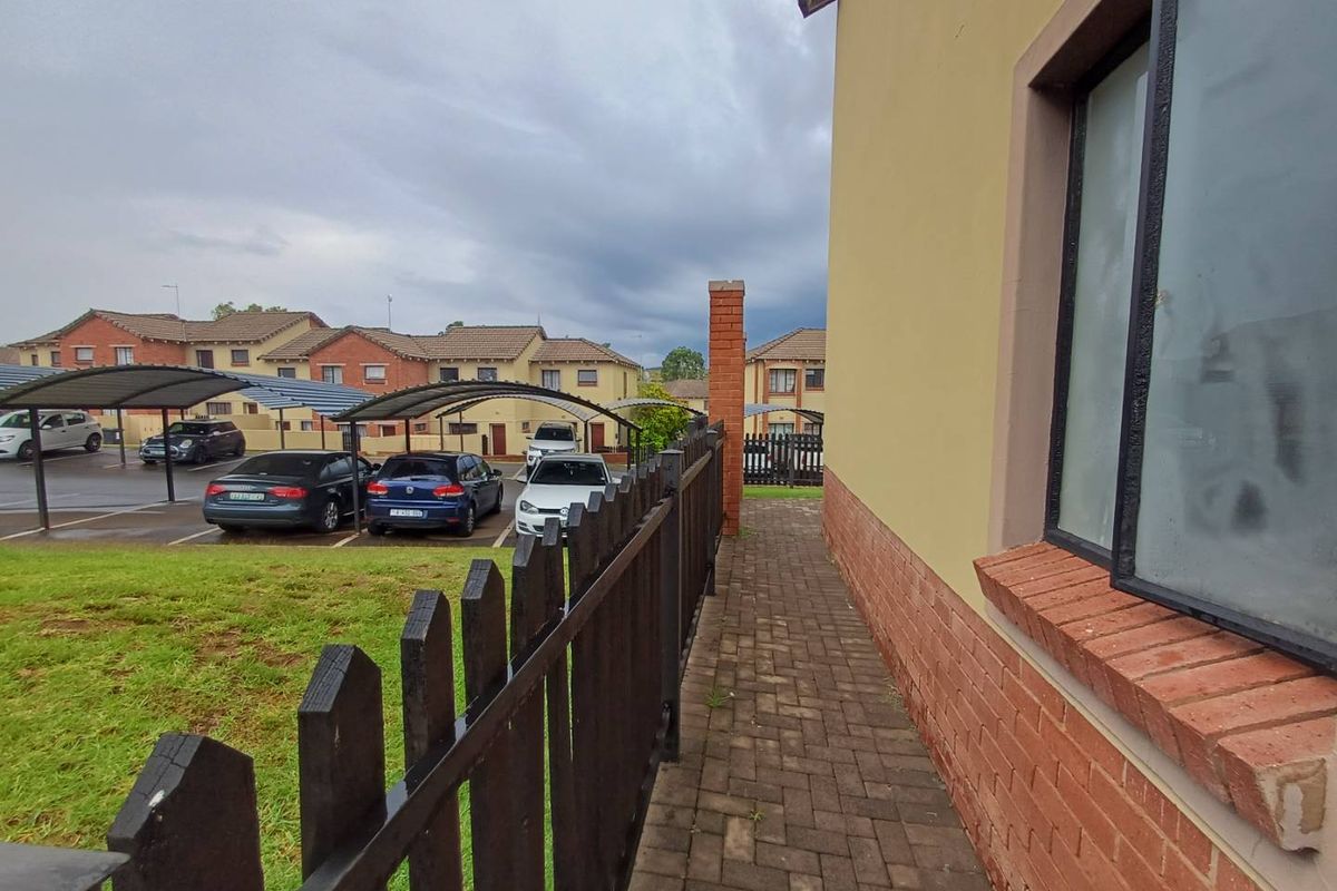 Exterior view of the townhouse side path featuring a paved walkway, brick base, and a dark timber fence overlooking the complex parking area.