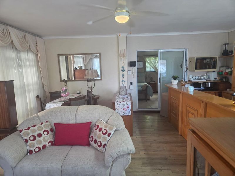 Open-plan living and kitchen area featuring laminate flooring, a ceiling fan, and a wooden breakfast bar connecting to the adjacent room.