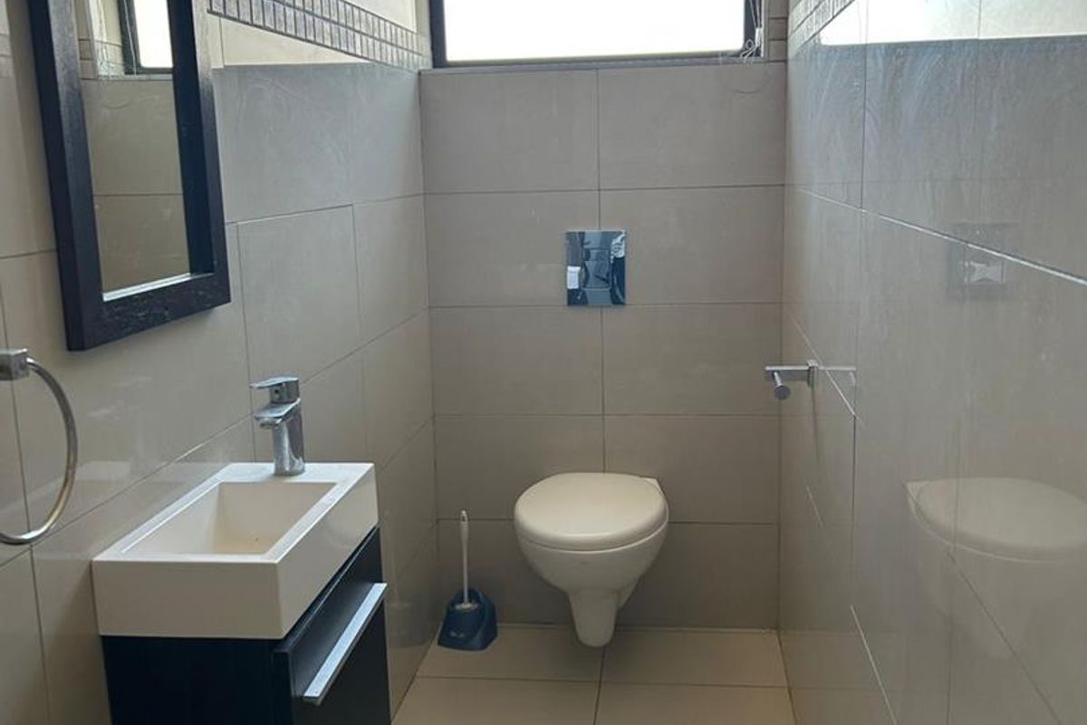 A modern guest bathroom featuring a wall-mounted toilet, a compact vanity with a basin, and neutral floor-to-ceiling wall tiles.