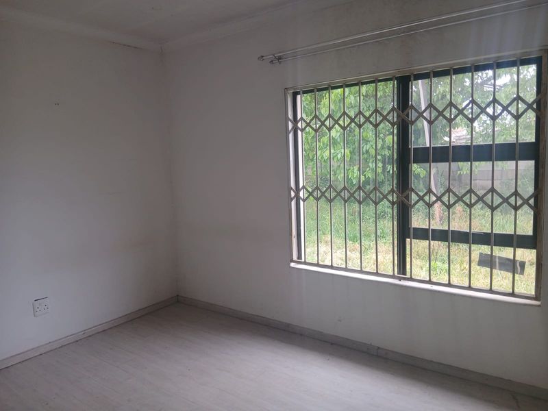 An empty bedroom featuring light-colored flooring, a window with a fitted security gate, and plain walls, offering a blank canvas for personalization.