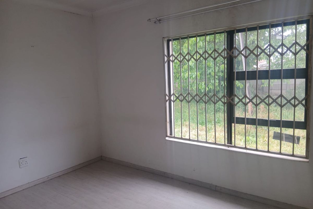 An empty bedroom featuring light-colored flooring, a window with a fitted security gate, and plain walls, offering a blank canvas for personalization.