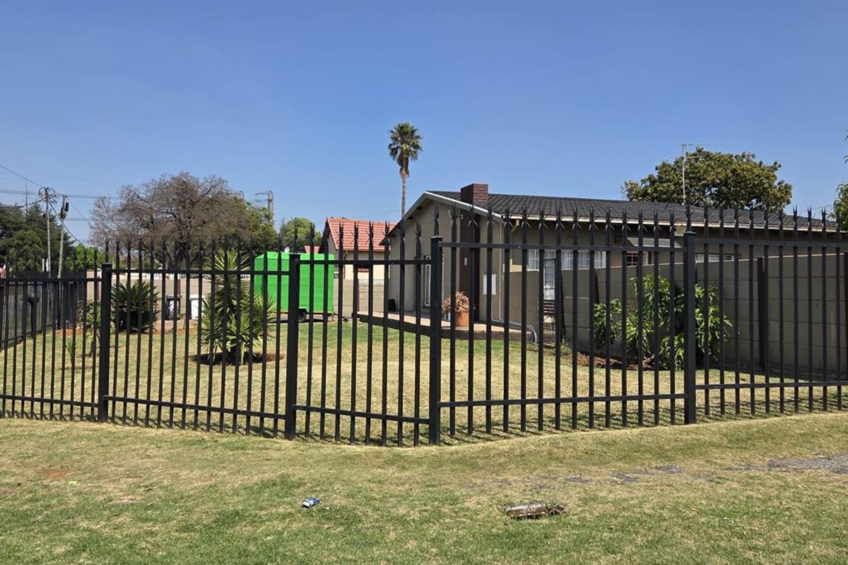 Rear view of the property featuring a spacious lawn, paved patio area, and secure metal perimeter fencing.