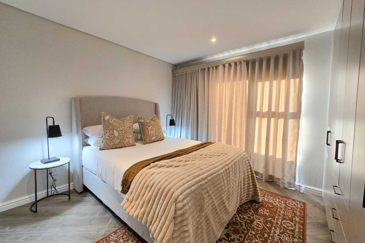 A well-maintained bedroom featuring neutral tones, wood-look flooring, built-in cabinetry, and floor-to-ceiling curtains leading to an outdoor area.