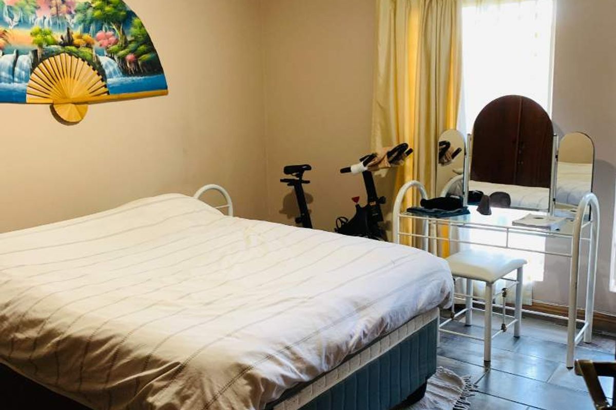 A standard bedroom featuring tiled flooring and natural light through a window with curtain rails.