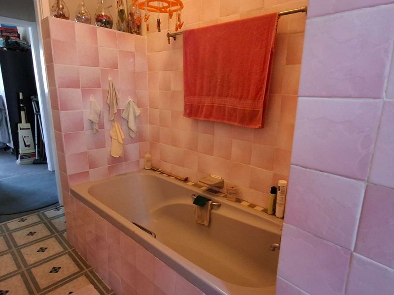 A bathroom featuring a built-in bathtub surrounded by dated pink ceramic wall tiles.