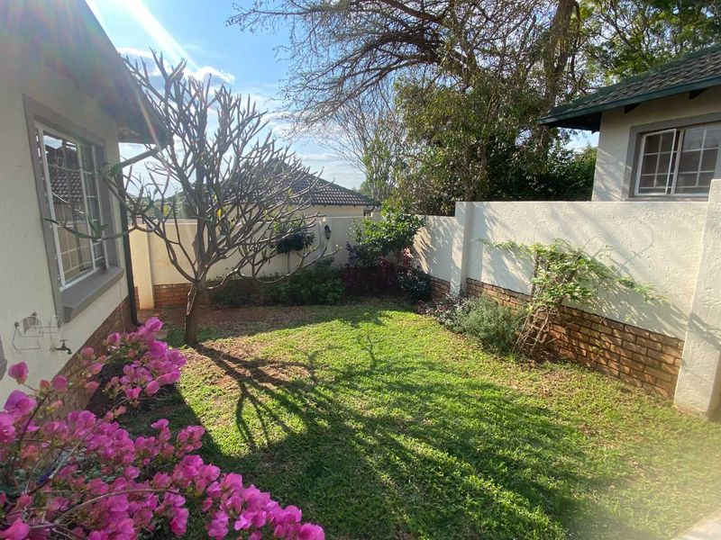 A private rear garden area featuring a manicured lawn, established trees, and a secure boundary wall with brick detailing.