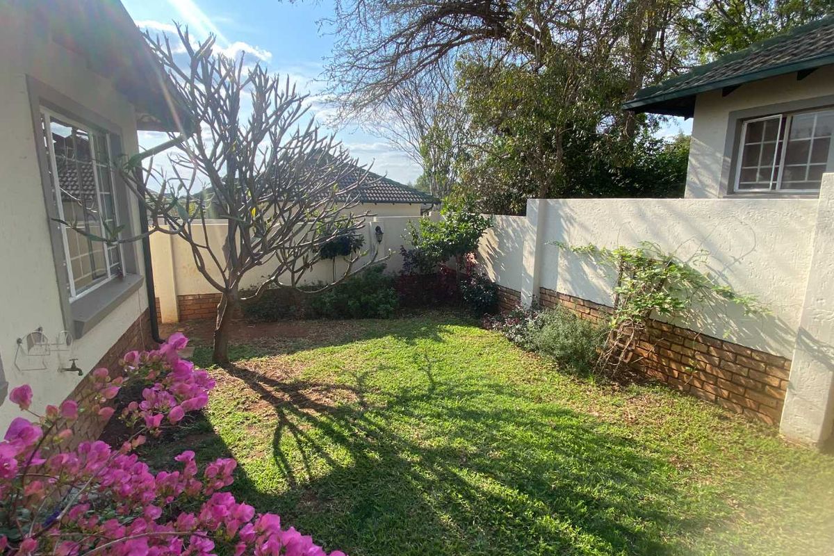 A private rear garden area featuring a manicured lawn, established trees, and a secure boundary wall with brick detailing.
