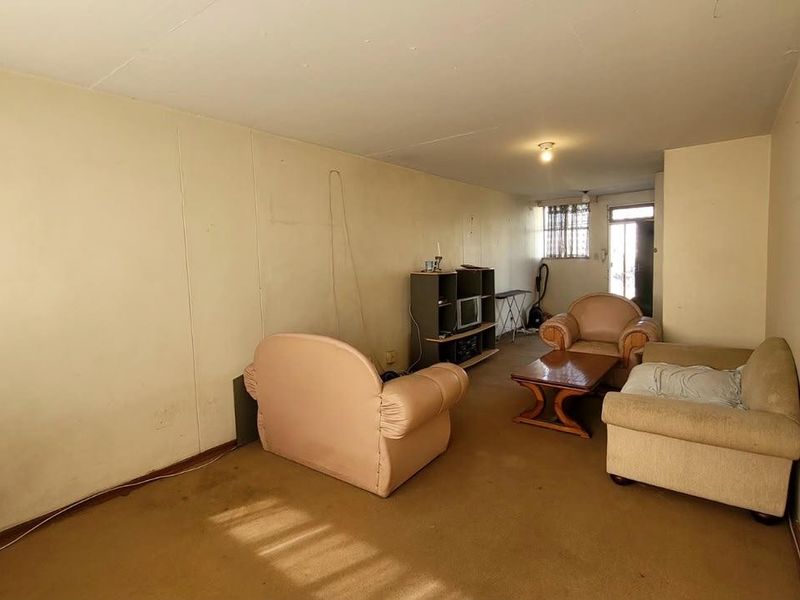 A living room area featuring carpeted flooring and security bars on the window, requiring cosmetic updates to improve its overall condition.
