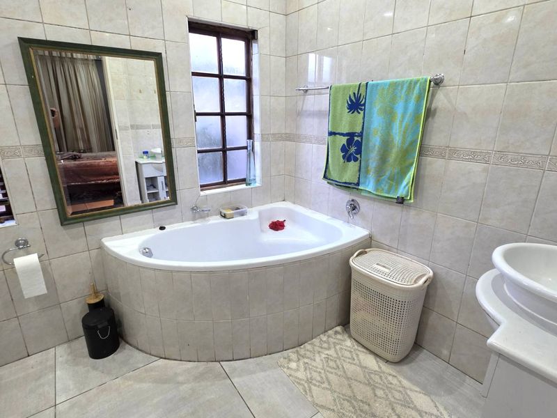 A functional bathroom featuring a corner bathtub, tiled wall and floor finishes, and a basin, offering a practical layout for daily use.