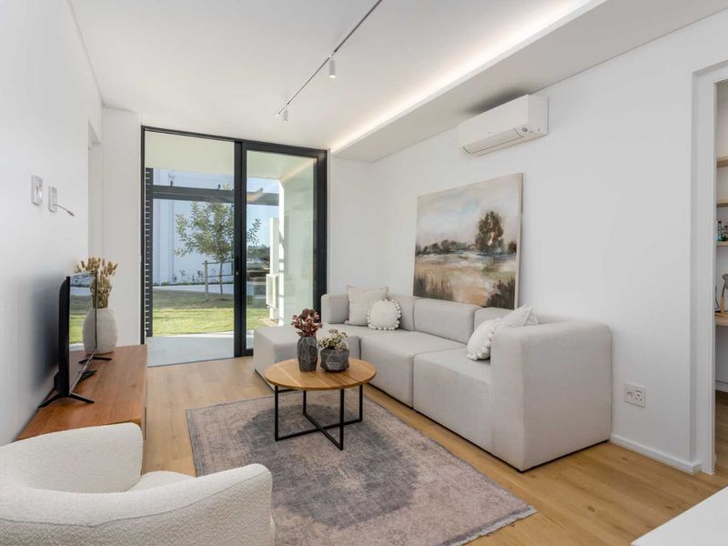 Modern living room featuring timber flooring, recessed ceiling lighting, a split-system air conditioner, and a sliding glass door leading to an outdoor area.