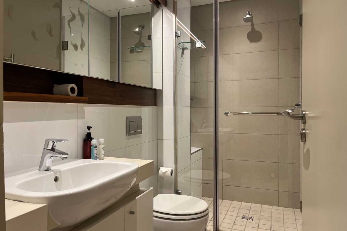 Modern bathroom featuring a glass-enclosed shower, wall-mounted toilet, and a vanity with integrated basin and mirrored cabinetry.