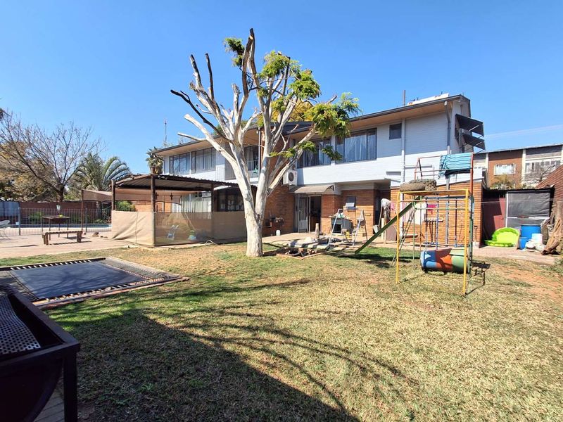 Rear view of the property featuring a spacious backyard, paved patio area, and two-story brick and cladding facade.