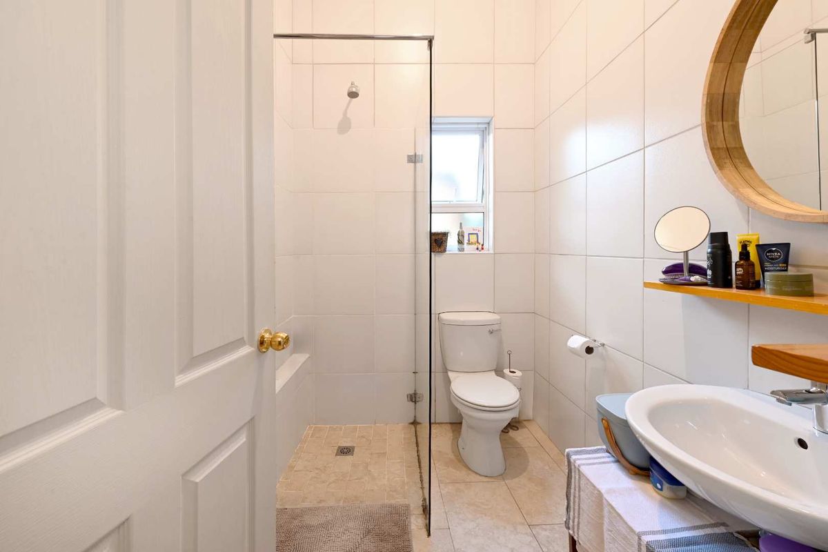 A clean, functional bathroom featuring a walk-in shower with a glass screen, a wall-mounted basin, and neutral floor-to-ceiling wall tiles.