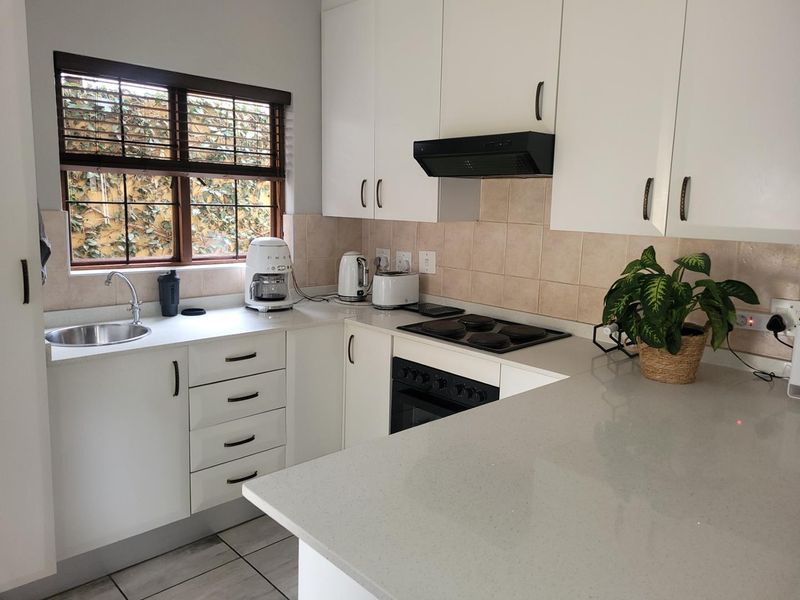 A clean and functional kitchen featuring white cabinetry, stone countertops, a built-in oven with hob, and a tiled backsplash.