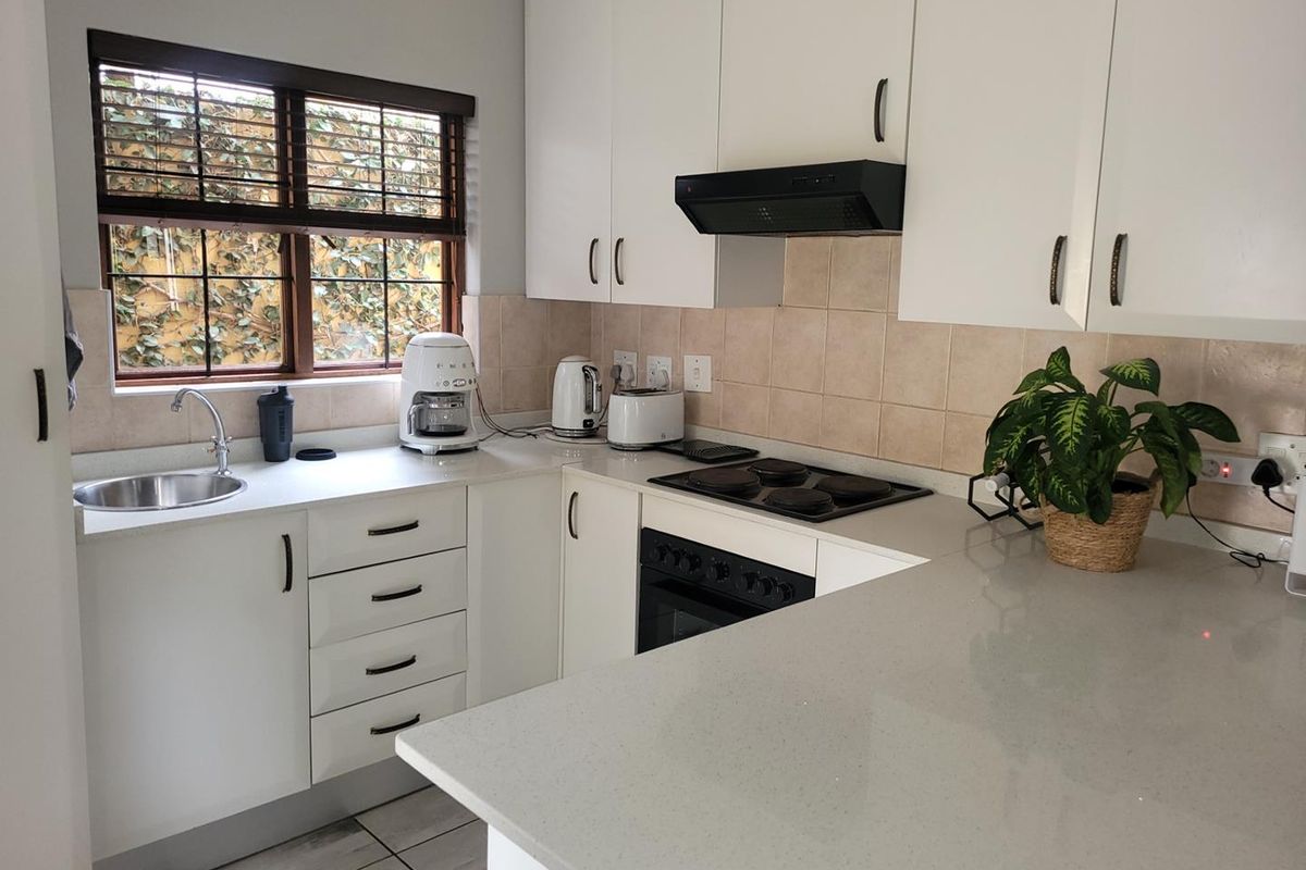 A clean and functional kitchen featuring white cabinetry, stone countertops, a built-in oven with hob, and a tiled backsplash.
