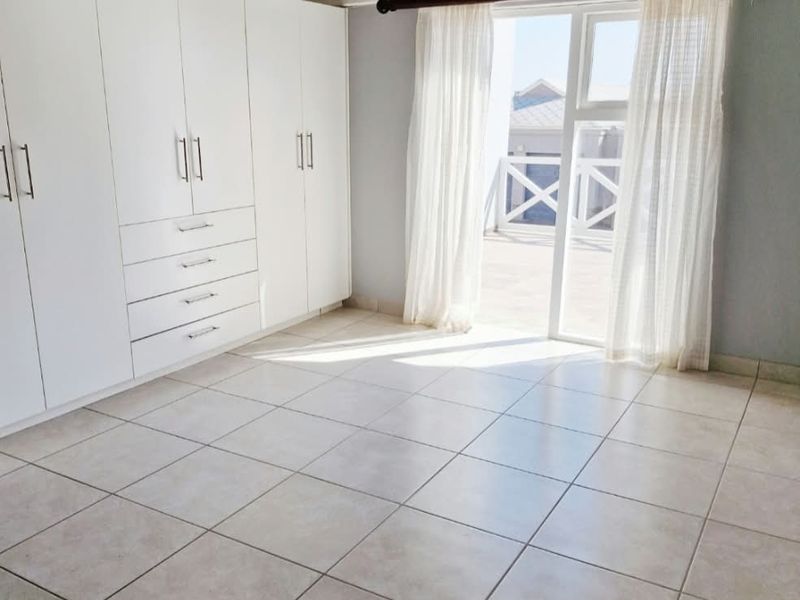 Spacious bedroom featuring high exposed timber rafters, built-in cupboards, tiled flooring, and direct access to an outdoor balcony through a sliding glass door.
