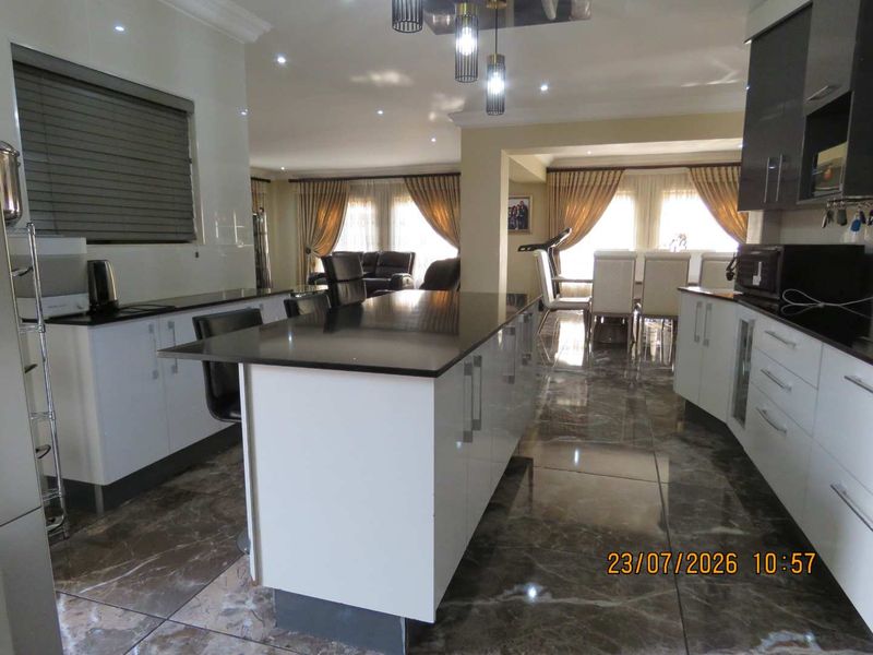 Spacious open-plan kitchen and dining area featuring a central island, modern glossy cabinetry, granite countertops, and polished porcelain floor tiles.