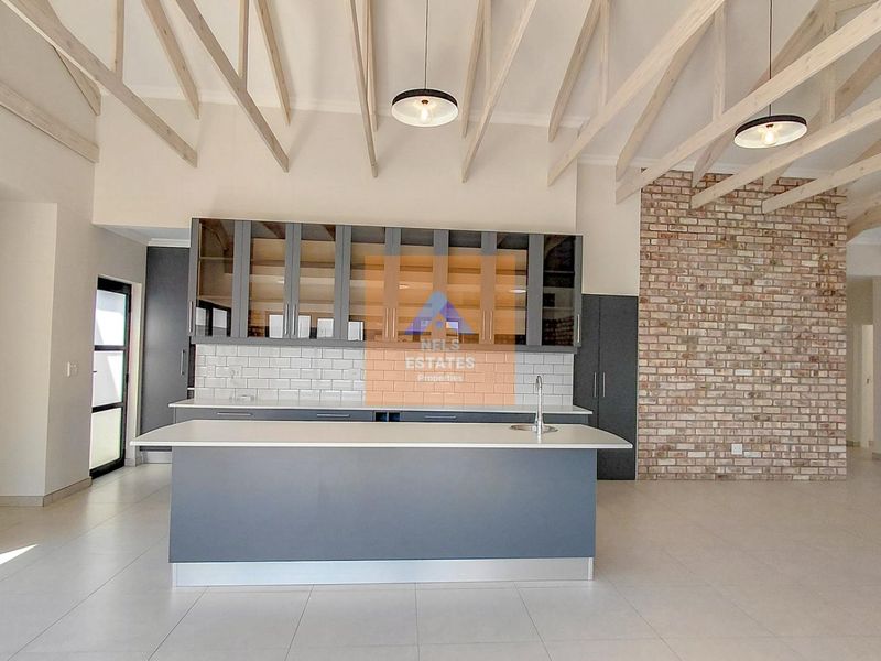Modern kitchen featuring a central island, subway tile backsplash, exposed brick wall, and high vaulted ceilings with exposed timber rafters.