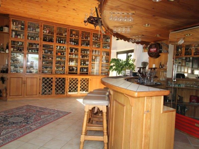 A dedicated home bar area featuring extensive built-in timber display cabinetry, a tiled bar counter, and warm wood-paneled ceilings.