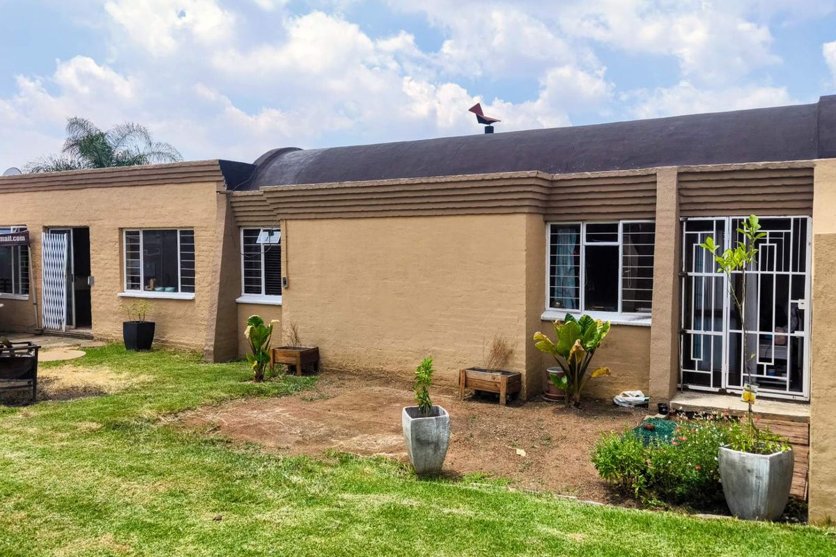 Rear view of the house featuring a textured facade, security gates, and a garden area with lawn and established planting.