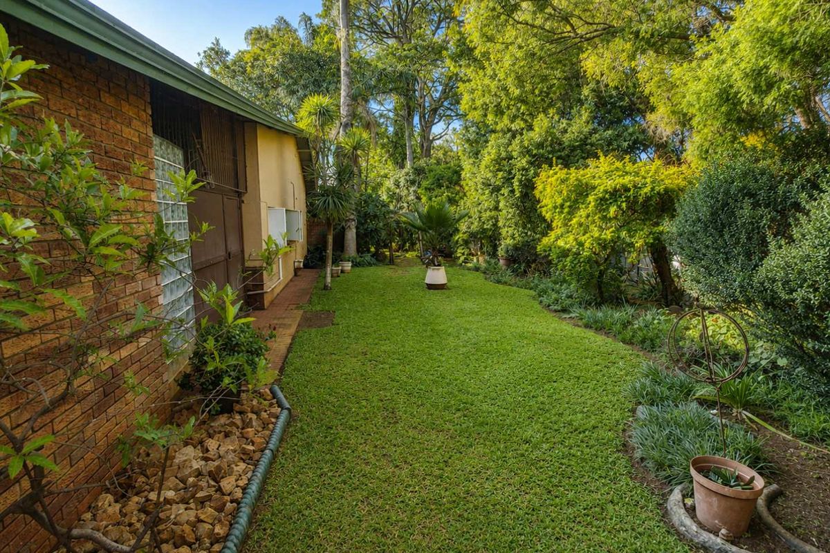 A well-maintained rear garden featuring a lush lawn, established trees, and a brick exterior wall of the house.