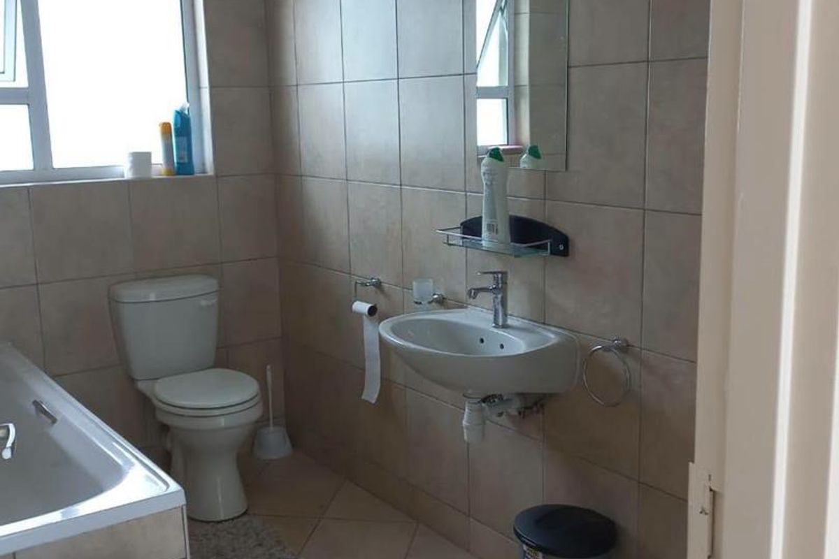 A functional bathroom featuring tiled walls and flooring, a bathtub, a wall-mounted basin, and a toilet, providing a standard layout for a townhouse.