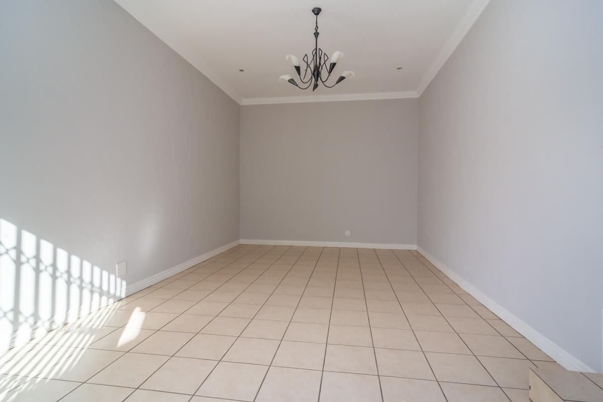 A bright, empty living area featuring neutral wall tones, tiled flooring, and a decorative ceiling light fixture.