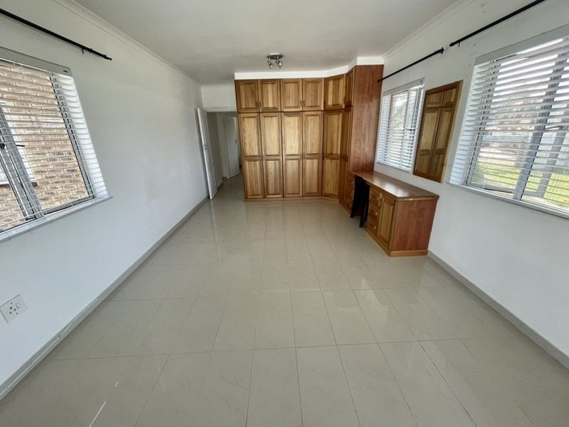 A spacious bedroom featuring tiled flooring, built-in wooden cabinetry, and a matching vanity desk, complemented by natural light from multiple windows.