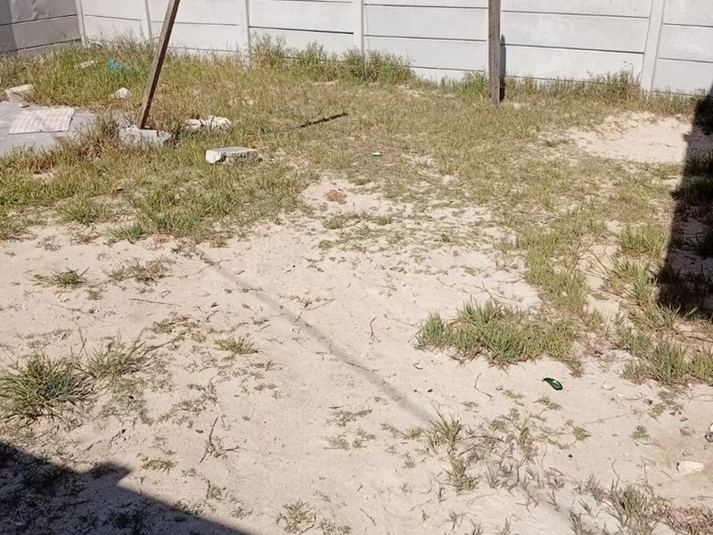 A rear garden area featuring a precast concrete boundary wall and an unmaintained sandy yard space.