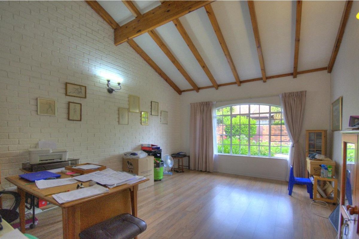 Spacious living area featuring exposed timber ceiling beams, a painted brick feature wall, and a large arched window overlooking the garden.
