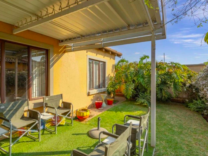 A covered patio area featuring a metal roof structure and artificial grass flooring, providing direct access to the garden through sliding glass doors.