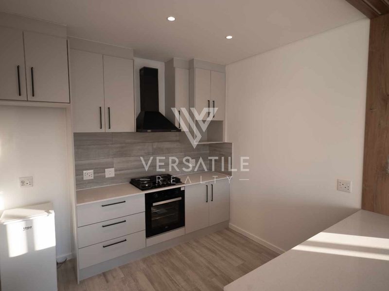 Modern kitchen featuring sleek grey cabinetry, built-in oven, extractor fan, and stone countertops, finished with light wood-look laminate flooring.