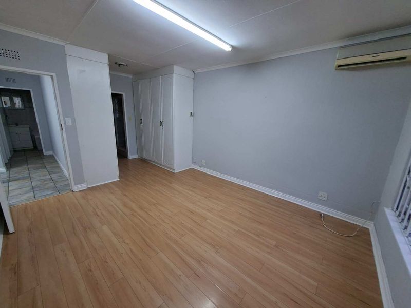 A spacious, empty bedroom featuring light laminate flooring, built-in cupboards, and an installed air conditioning unit.