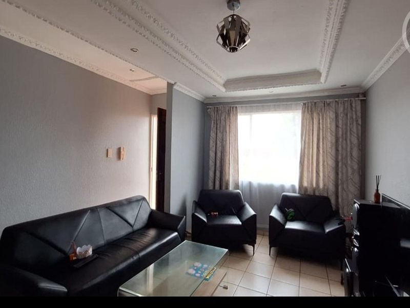 A living room featuring tiled flooring, decorative ceiling cornicing, and a recessed ceiling design, providing a functional and neutral space.