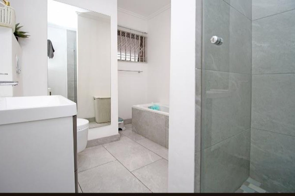 A modern bathroom featuring a glass-enclosed shower, a built-in bathtub, a vanity basin, and large-format floor tiles.