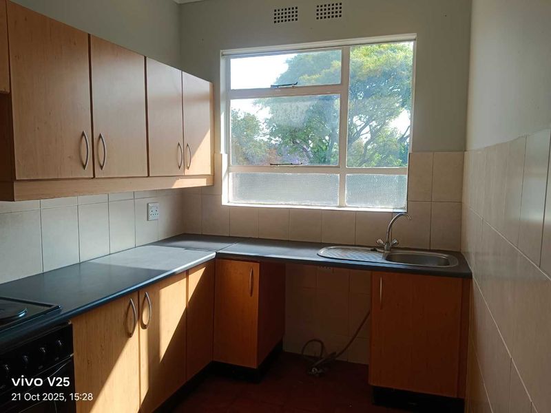 A functional kitchen featuring laminate cabinetry, tiled backsplash, and a stainless steel sink, offering a blank canvas for potential modern updates.