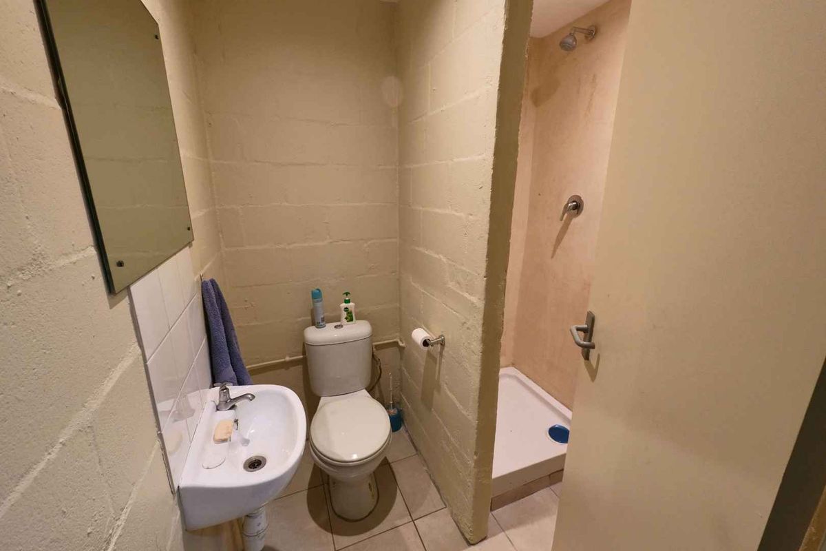 A functional bathroom featuring a wall-mounted basin, toilet, and a separate shower enclosure with basic finishes and exposed blockwork walls.