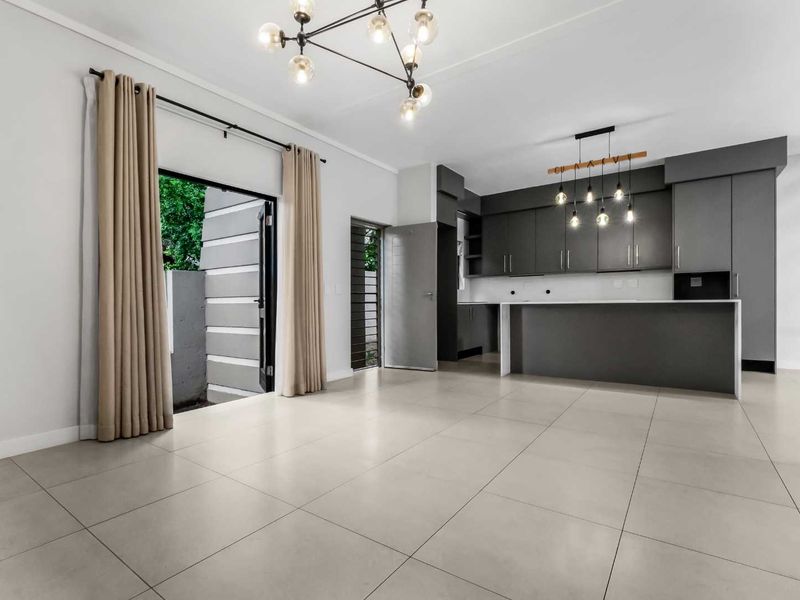 Modern open-plan living and kitchen area featuring sleek grey cabinetry, a central island, large format floor tiles, and direct access to the outdoor space.