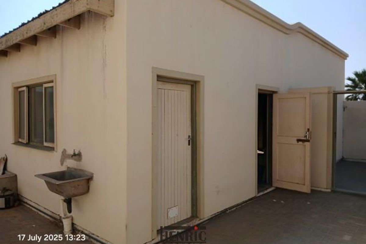 Exterior view of the rear building facade featuring a utility sink, multiple access doors, and paved outdoor area.