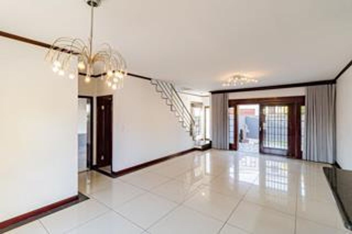 Spacious open-plan living area featuring polished tile flooring, a modern staircase with metal railing, and large sliding glass doors leading to the exterior.
