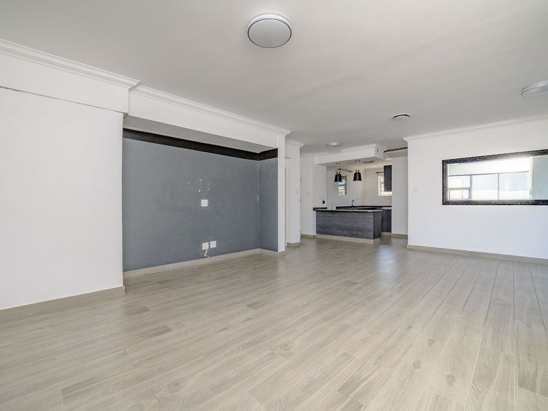 Spacious open-plan living area featuring light wood-look laminate flooring, a modern kitchen island, and a dedicated feature wall, offering a bright and versatile layout.