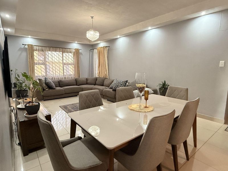Spacious open-plan living and dining area featuring polished tiled flooring, recessed ceiling lighting, and large windows with security bars.