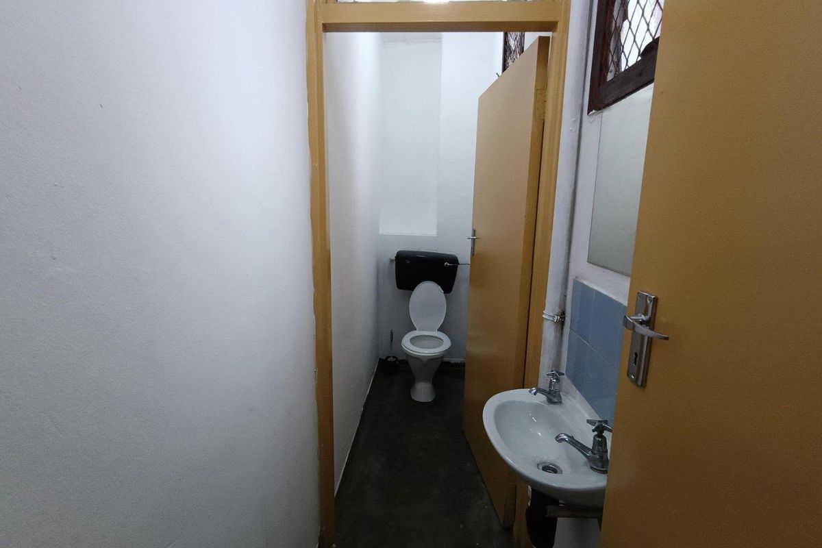 A compact industrial-style bathroom featuring a wall-mounted basin, toilet, and basic finishes, presenting an opportunity for modernization and cosmetic updates.