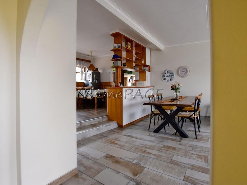 Open plan dining and kitchen area featuring a built-in timber room divider, tiled flooring, and a raised transition between spaces.