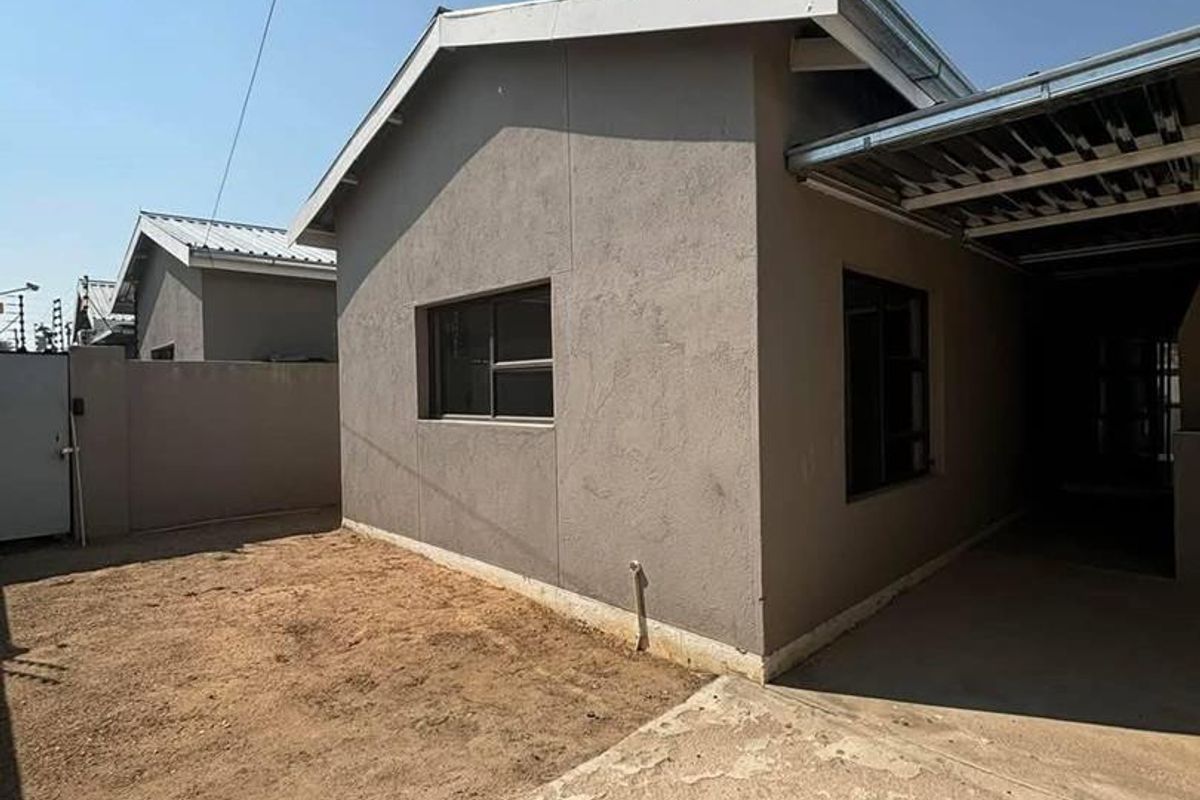 Exterior view of the townhouse featuring a concrete driveway, side access, and a compact garden area with a neutral rendered facade.