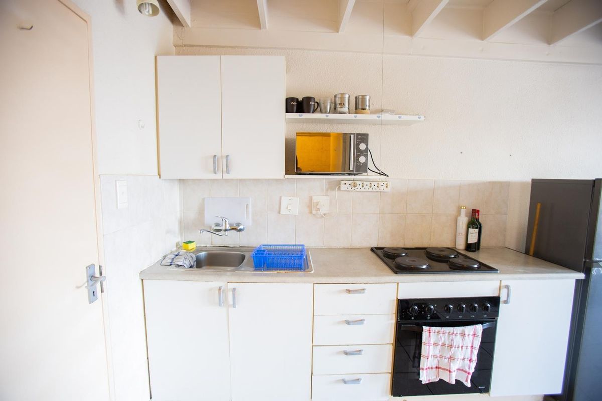 Compact kitchen featuring white cabinetry, a built-in oven with electric hob, stainless steel sink, and tiled backsplash.