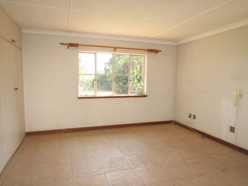 An empty bedroom featuring tiled flooring, a built-in cupboard, and a steel-framed window, offering a blank canvas for renovation.